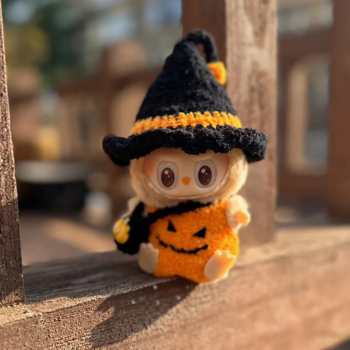Small Halloween-themed labubu have a seat toy with a black witch hat and orange pumpkin outfit on a wooden surface.