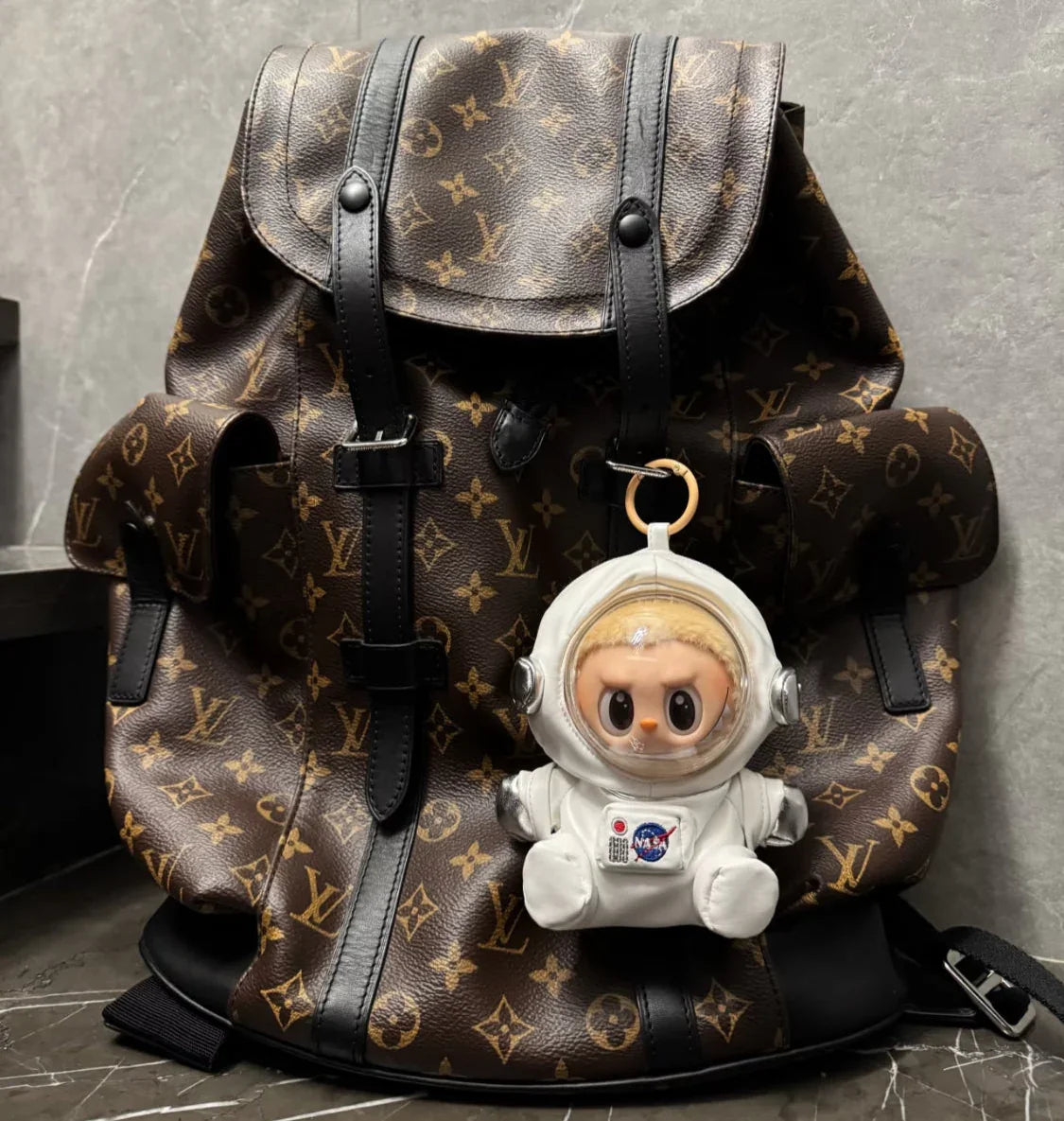 Designer backpack with a space-themed keychain on a gray surface