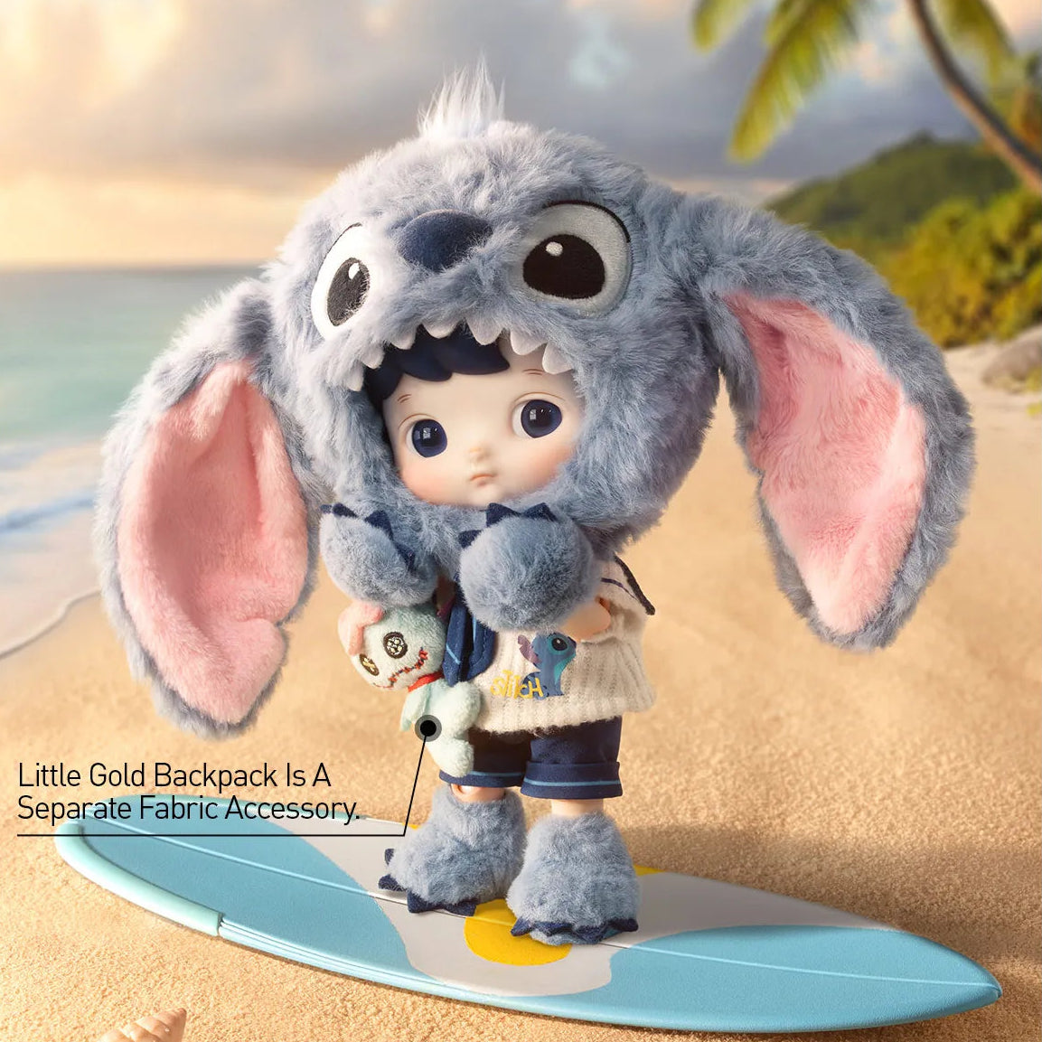 A plush doll or toy character with a large gray bunny ears hood and pink inner ears stands on a light blue surfboard on a sandy beach. The character wears a white top and dark shorts.