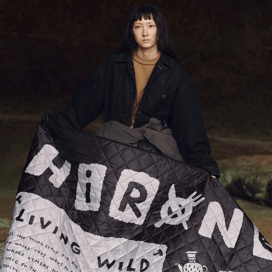 Person holding a quilt with text and graphics on a dark background