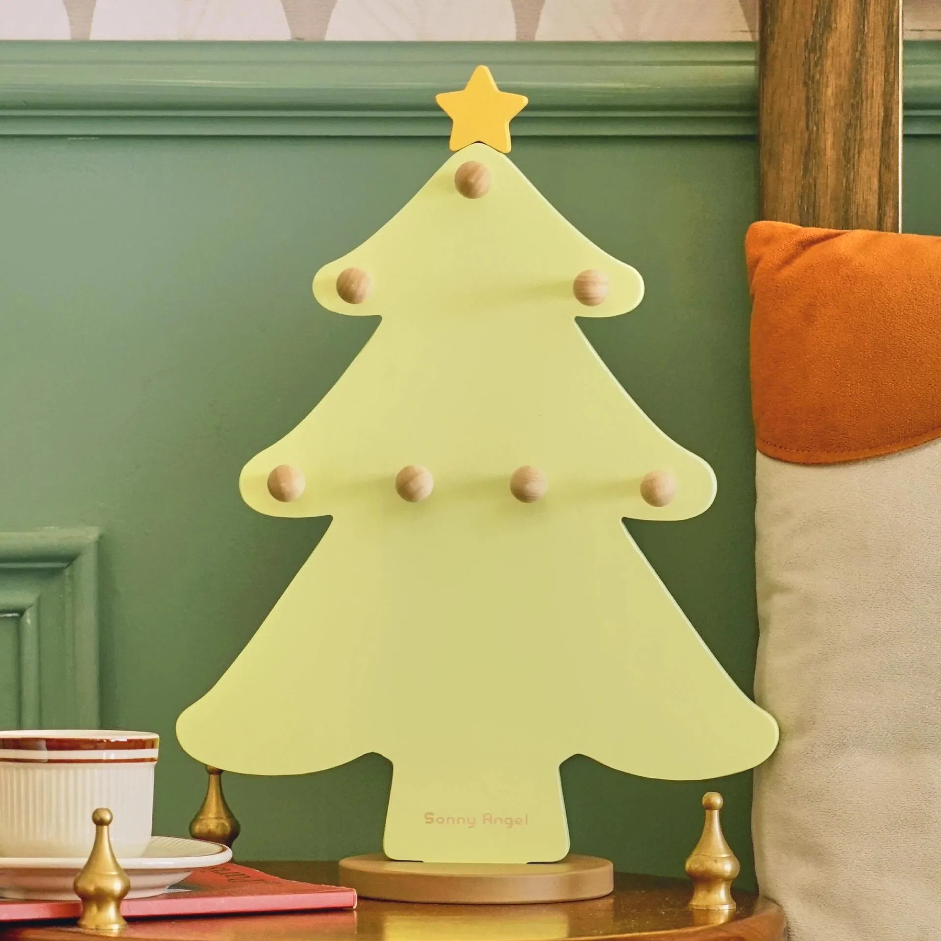 Decorative Christmas tree-shaped item on a table against a green wall with a patterned wallpaper.