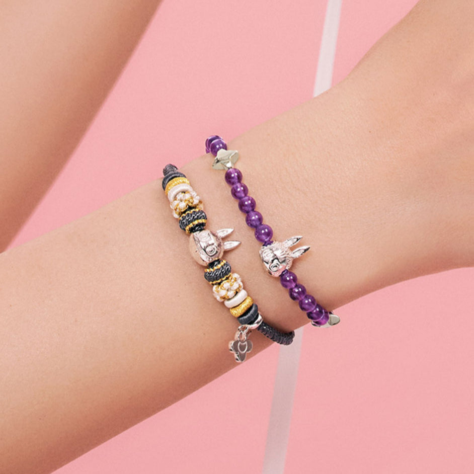 Two beaded bracelets on a wrist against a pink background