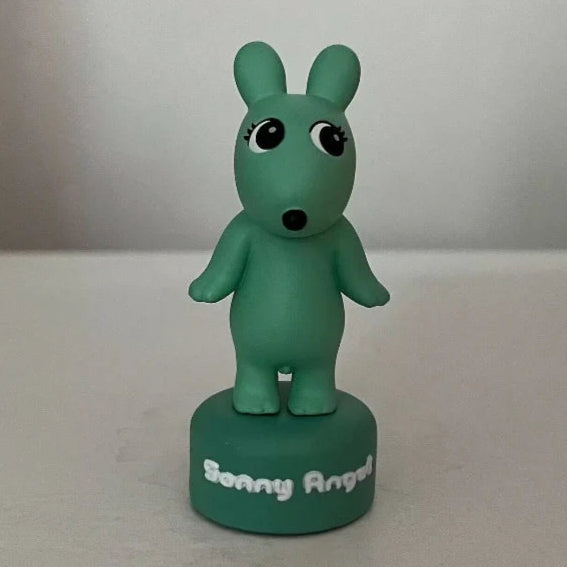Green cartoon-like figurine on a white surface with a plain background