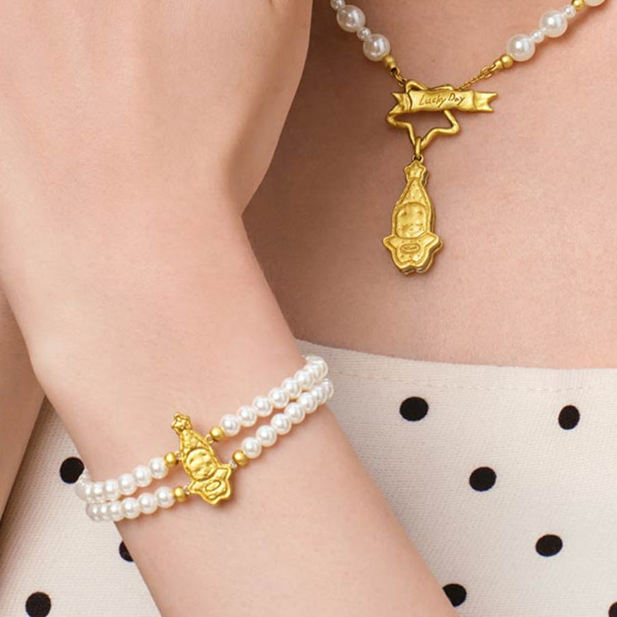 Pearl necklace and bracelet set with gold Buddha charms on a person wearing a polka dot dress.