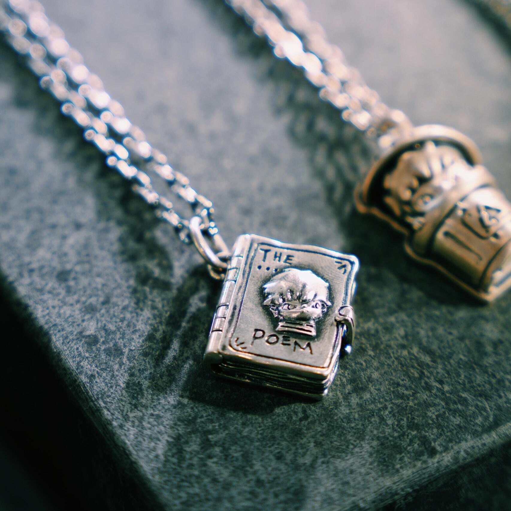 Silver necklace with a book-shaped pendant on a textured surface
