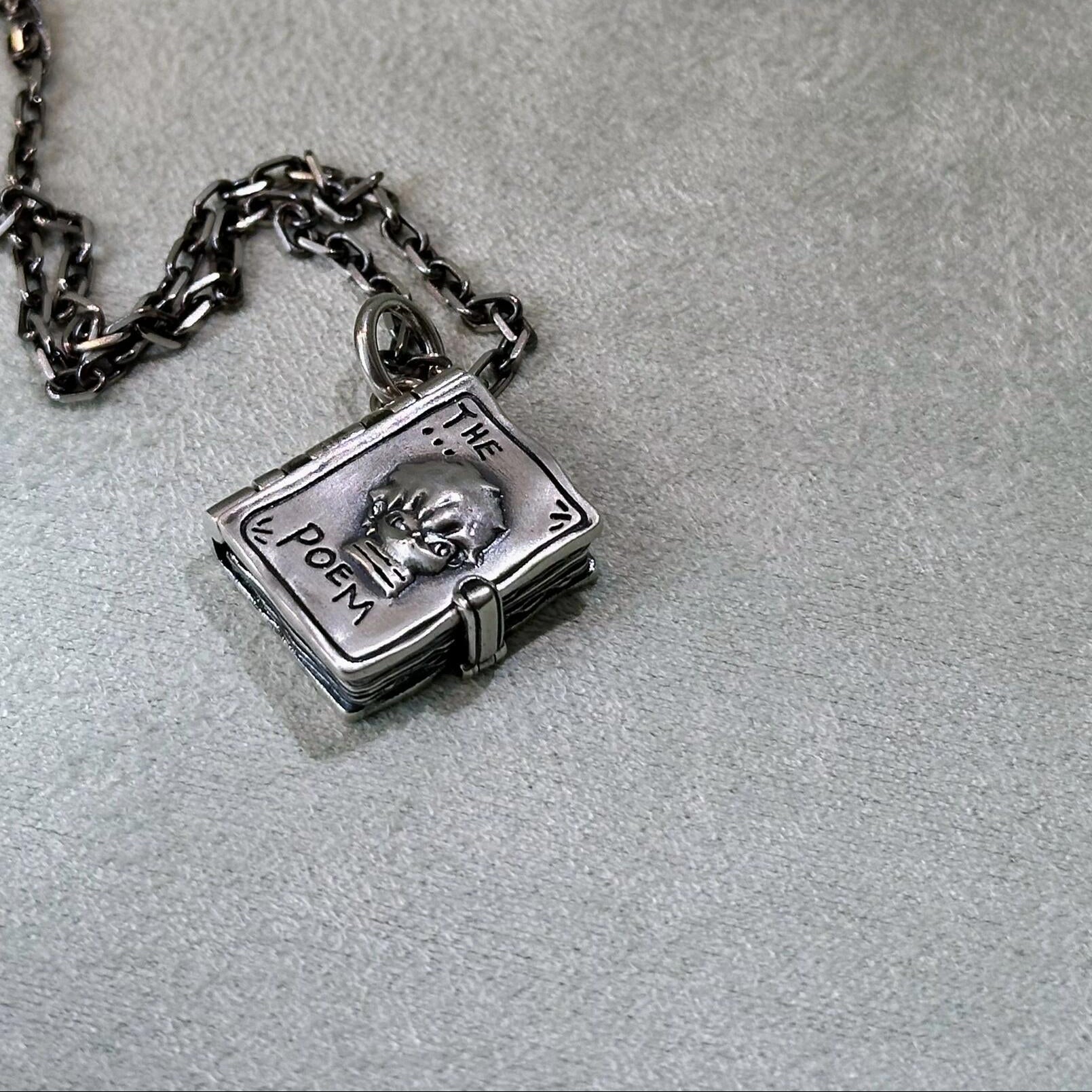 Silver necklace with a book-shaped pendant on a light gray surface.