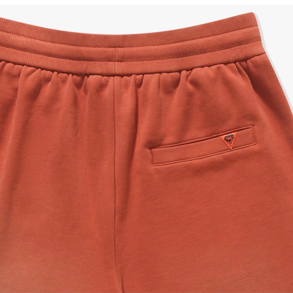 Close-up of terracotta orange sweatpants showing the elastic waistband and a side pocket with a small embroidered logo.