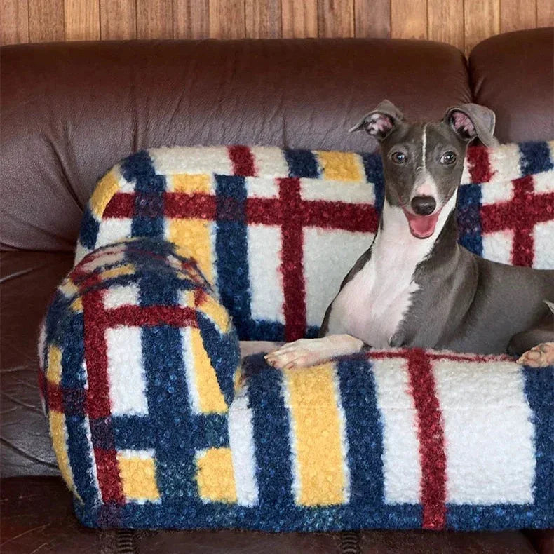 Dog sitting on a colorful geometric-patterned blanket on a brown couch.
