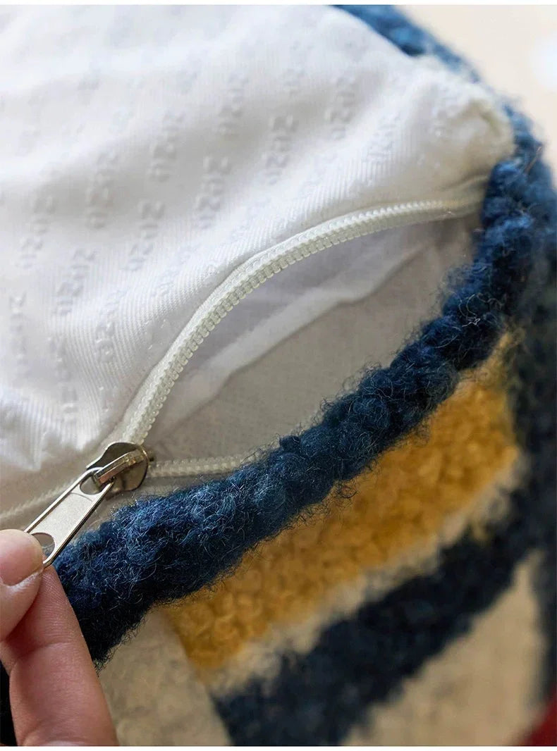 Close-up of a zipper on a striped fabric pillow with a hand holding it open.