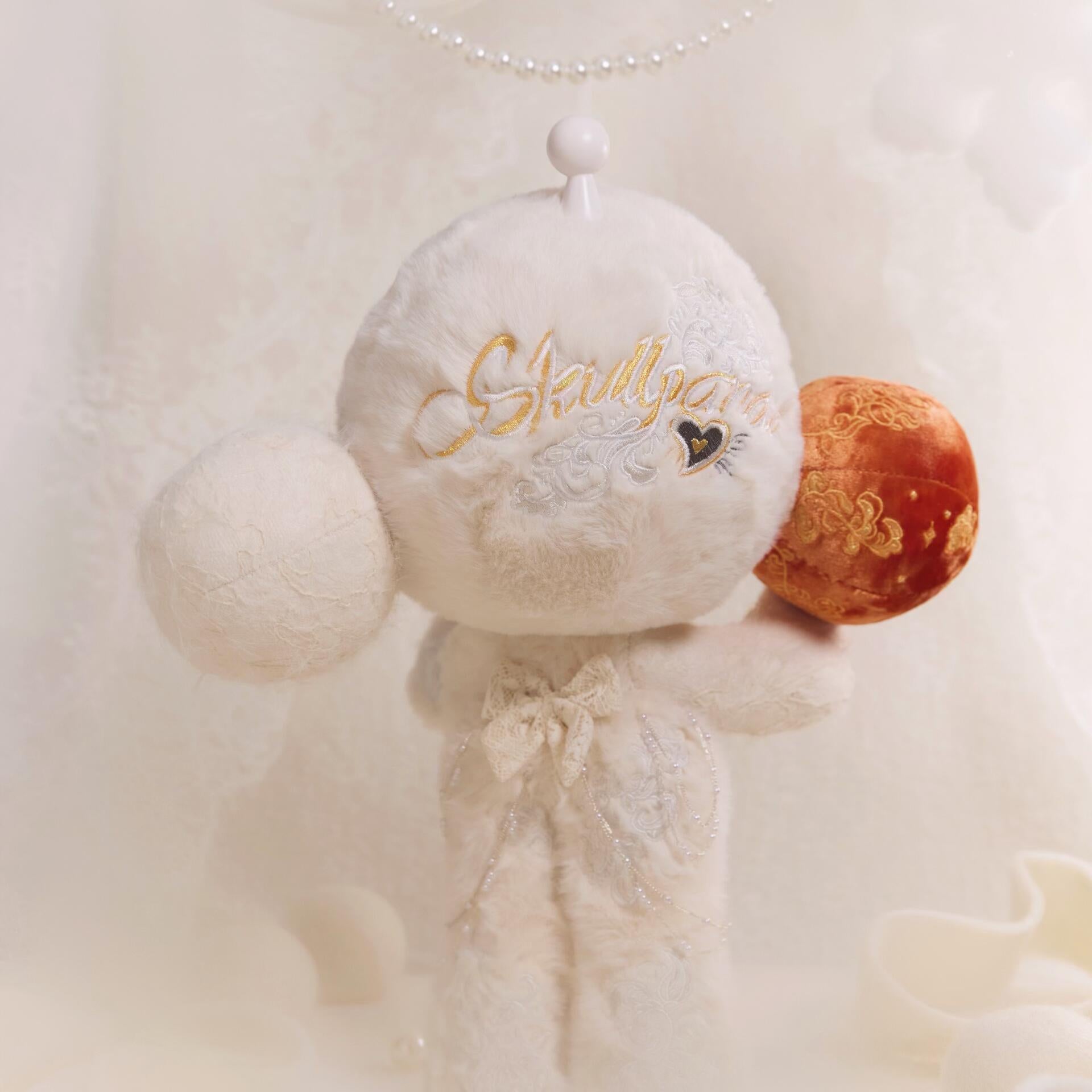 White plush toy with gold text and orange heart on a soft white background