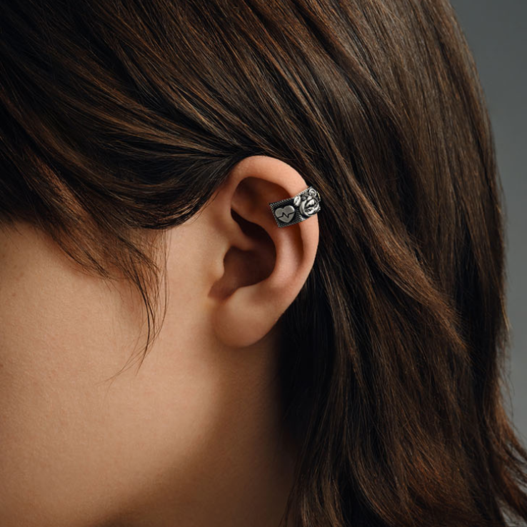 Close-up of an ear wearing a decorative earring with dark hair and blurred background