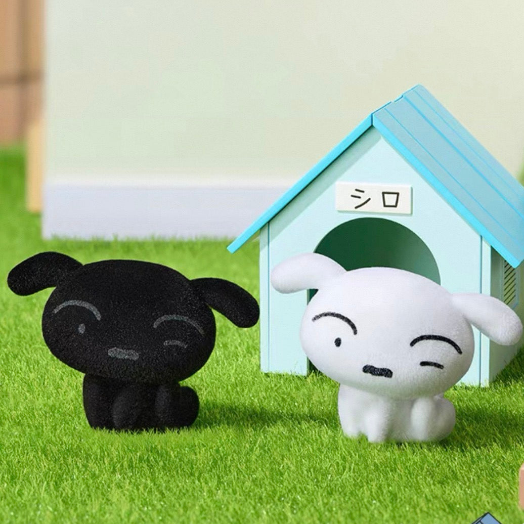 Two small plush dog figures, one black and one white, posed beside a light blue dog house on a green artificial grass surface.
