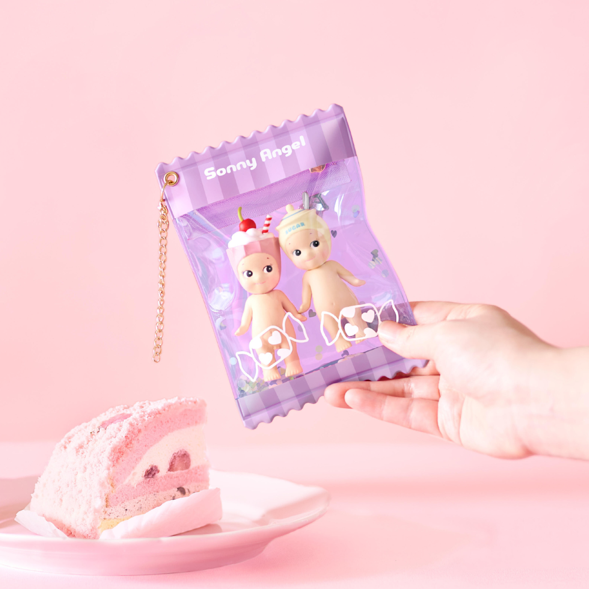 Hand holding a clear pouch with two dolls inside against a pink background