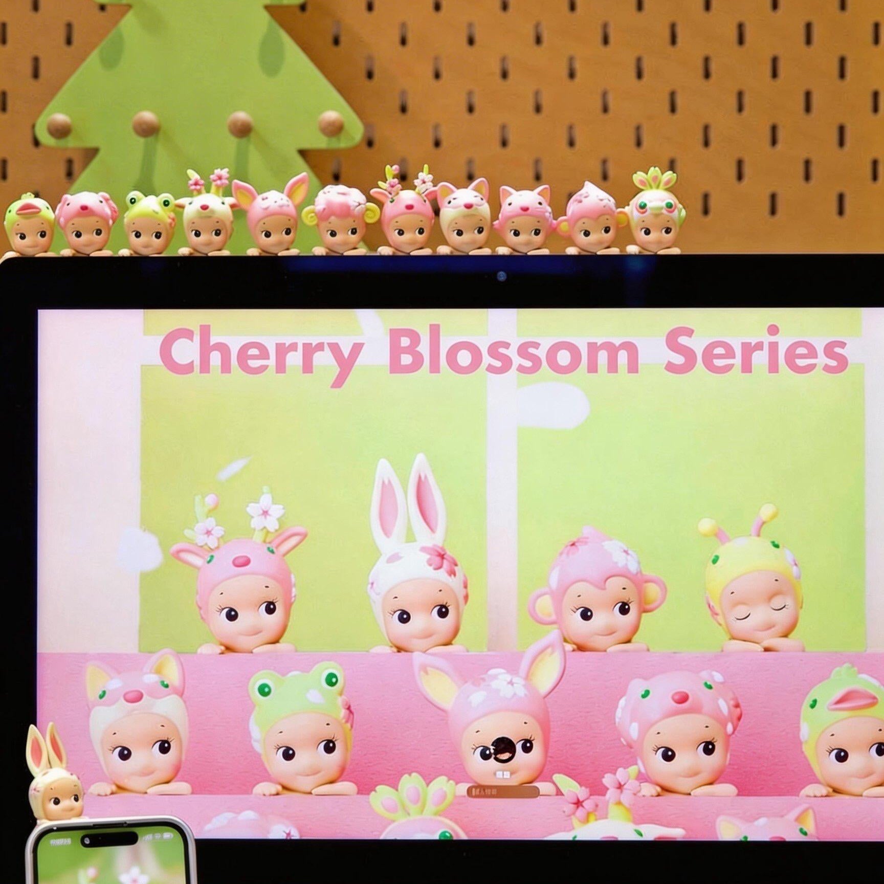 Collection of small figurines with a 'Cherry Blossom Series' display in front of an Apple computer.