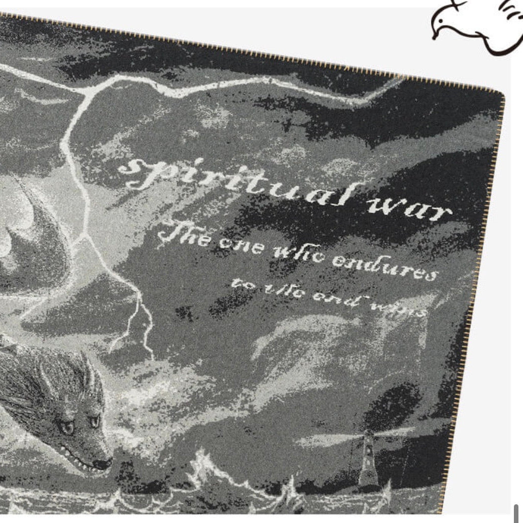 A square printed item, likely a pouch or cover, featuring a black and white gothic illustration of a dragon and stormy clouds with the text 'spiritual war' and 'The one who endures to see and write'.