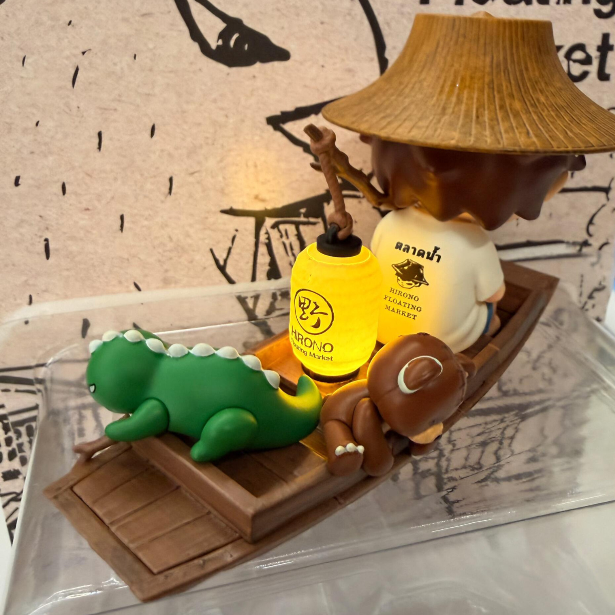 Figurine of a person in a boat with a hat, bottle, and frog on a white background