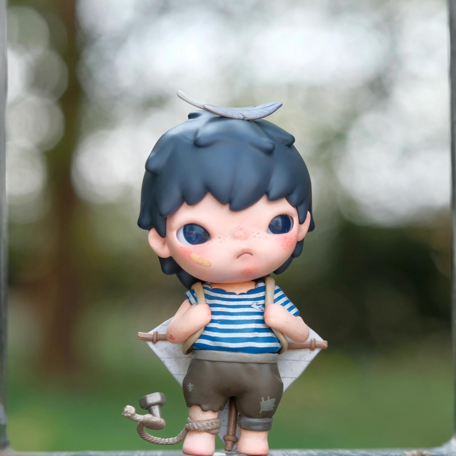 Toy figure with blue hair and a striped shirt against a blurred natural background