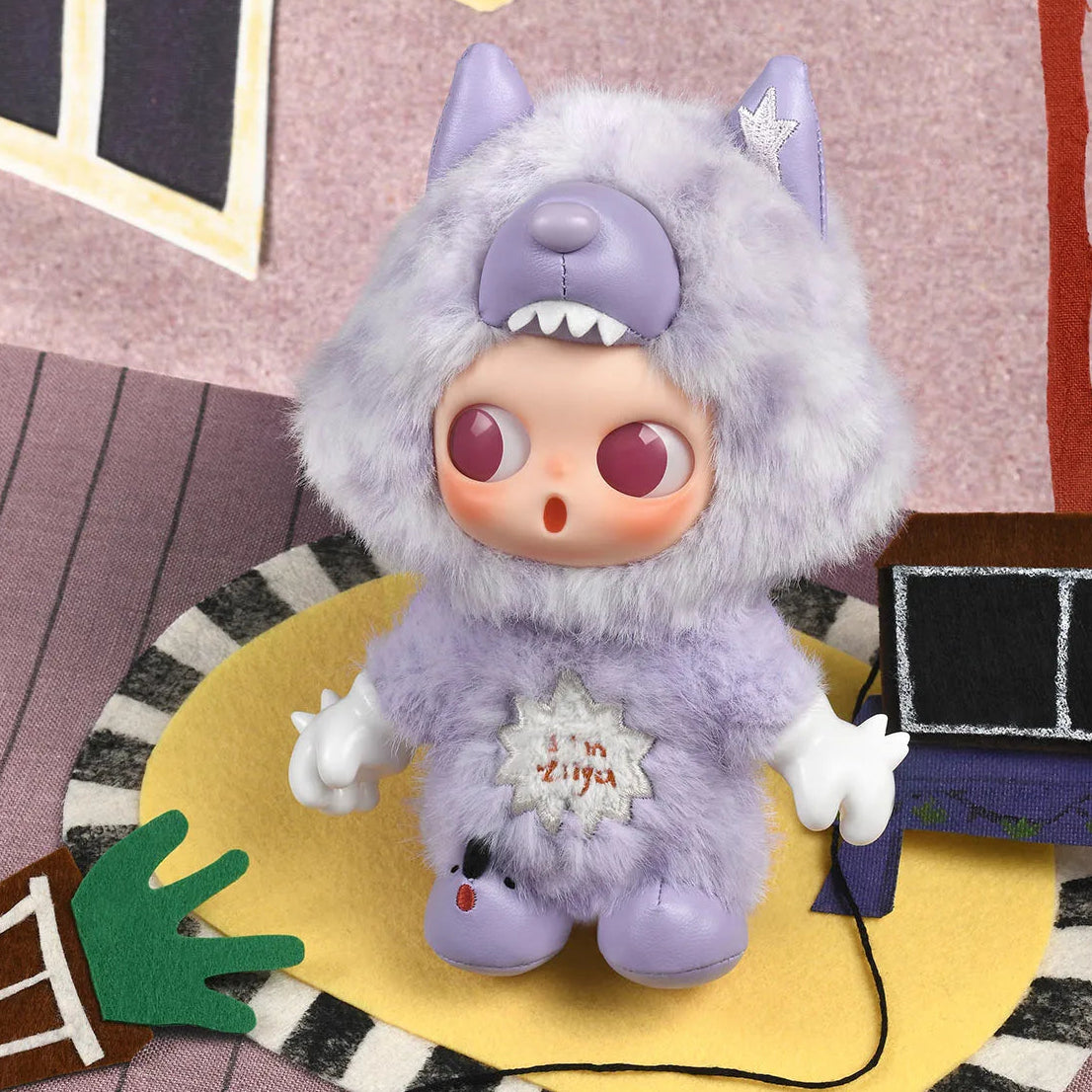 Purple plush toy with large eyes and a surprised expression on a colorful rug.