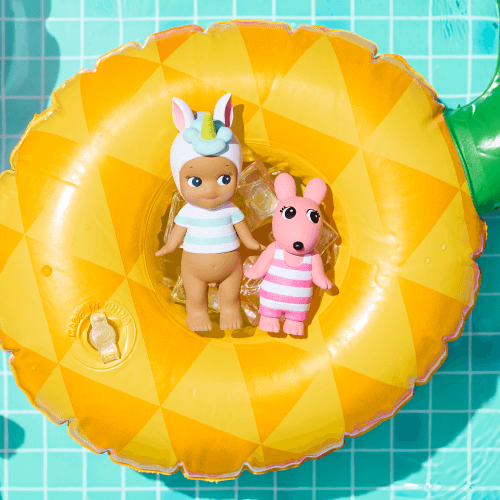 Two small figurines on a pineapple-shaped inflatable ring with flowers and a pink bowl in the background.