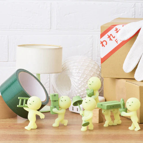 Small green figures with tools on a wooden surface, next to a box and gloves.