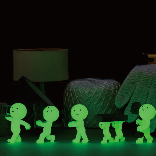 Glowing green figures on a dark surface with a lamp and chair in the background.