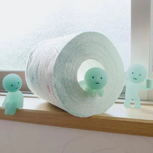 Roll of toilet paper with two small green characters on a windowsill.