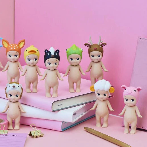 Set of small figurines with animal hats on a pink surface with stationery items.