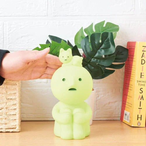 Glowing green character-shaped container with a plant on a wooden surface next to books.