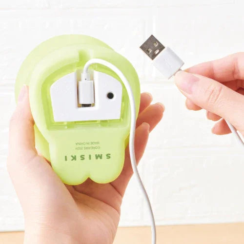 Green apple-shaped device with USB cable being plugged into it, held by a hand.