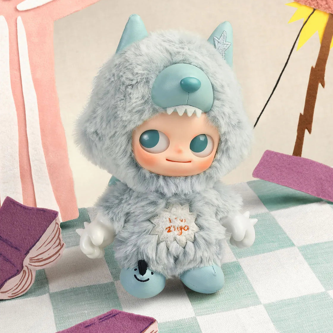 Plush toy with blue face and gray fur sitting on a checkered tablecloth.
