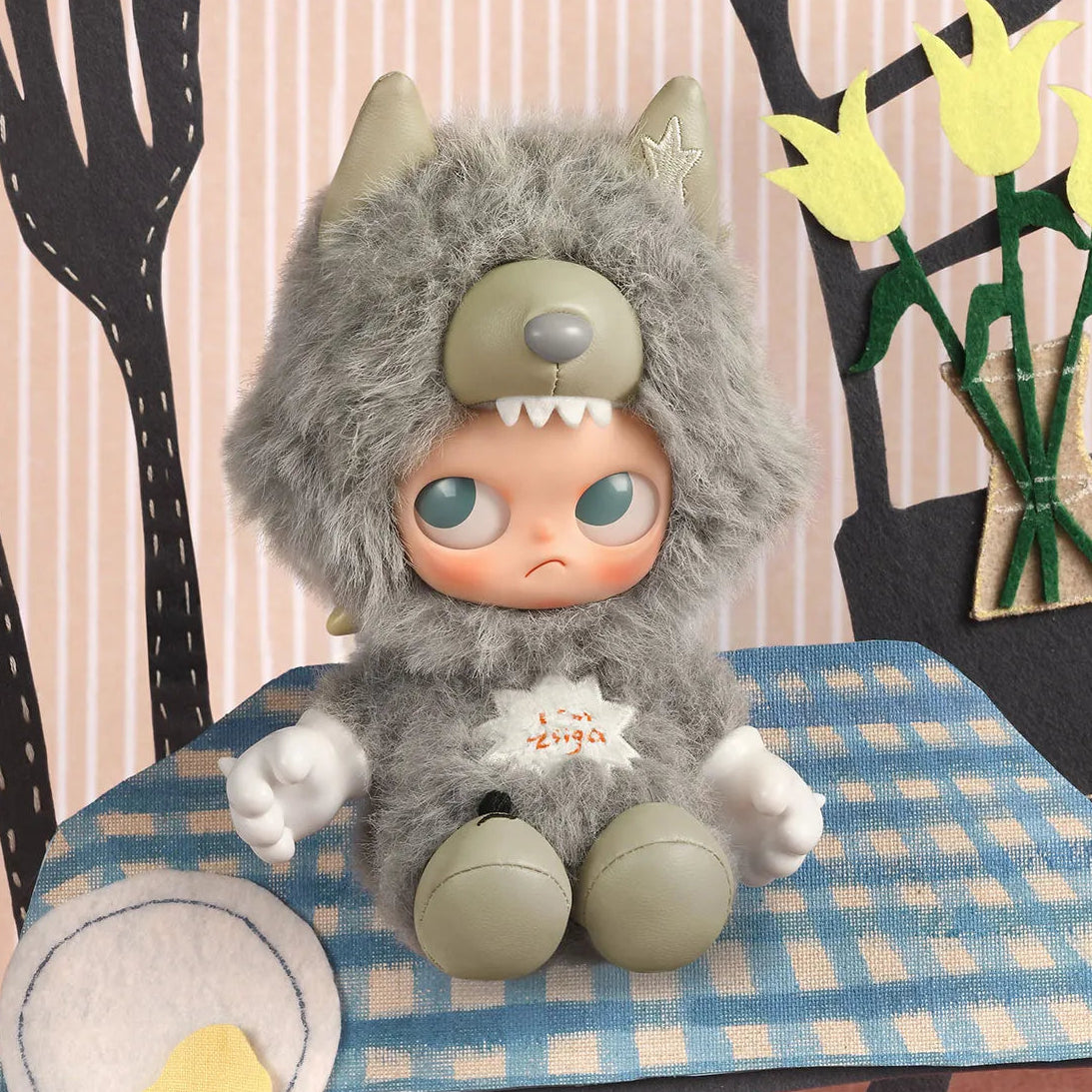 Plush toy with a gray furry costume sitting on a table with a checkered tablecloth.