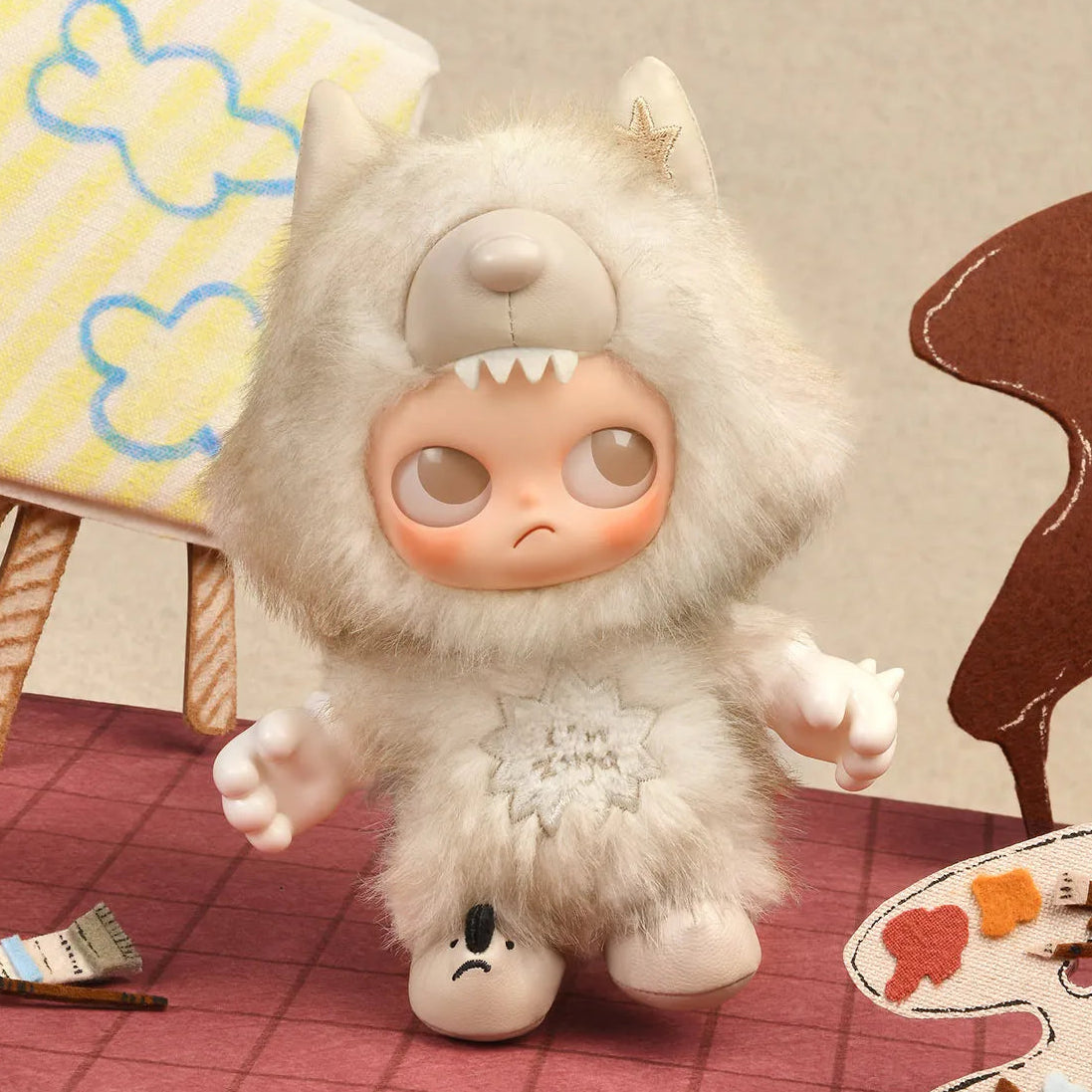 Plush toy with a sad expression on a checkered floor with art supplies.